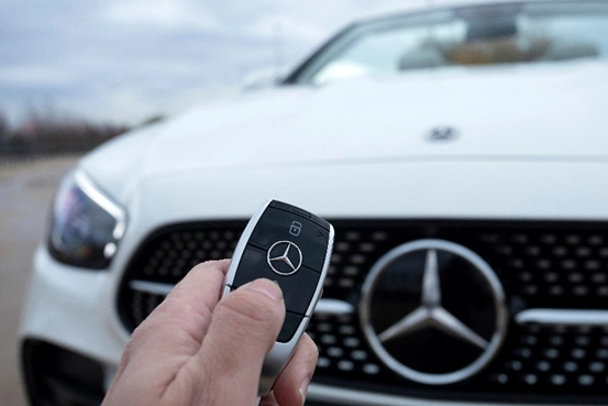 hand holding a Mercedes key in front of Mercedes