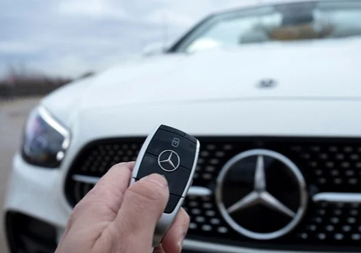 hand holding a Mercedes key in front of Mercedes